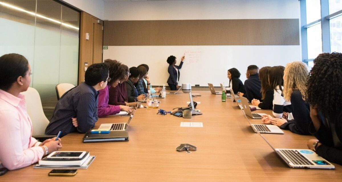 people on conference table looking at talking woman