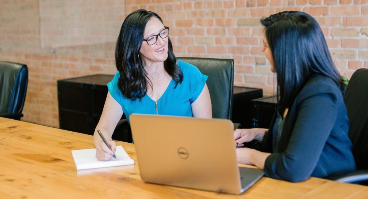 woman in teal t-shirt sitting beside woman in suit jacket