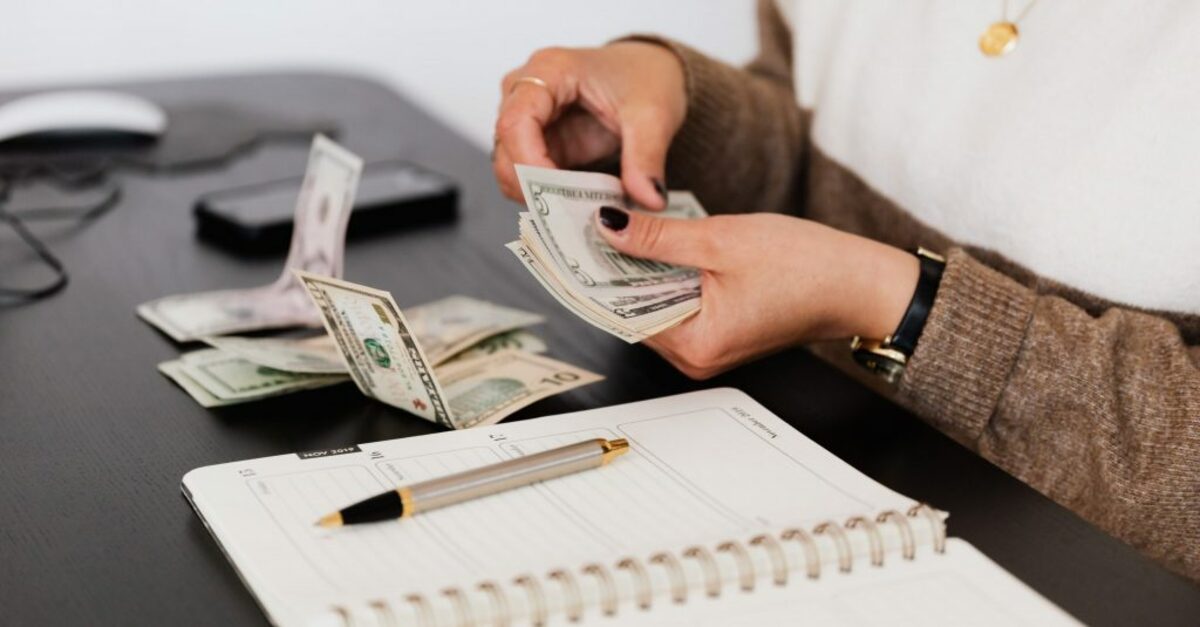 Crop payroll clerk counting money while sitting at table