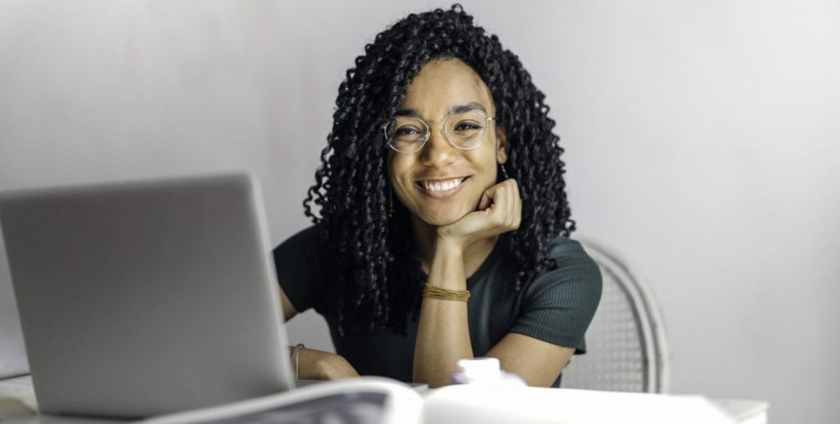 Happy ethnic woman sitting at table with laptop