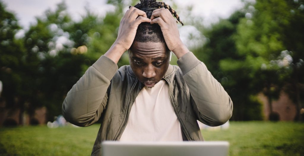 Stressed black male entrepreneur working on laptop in park