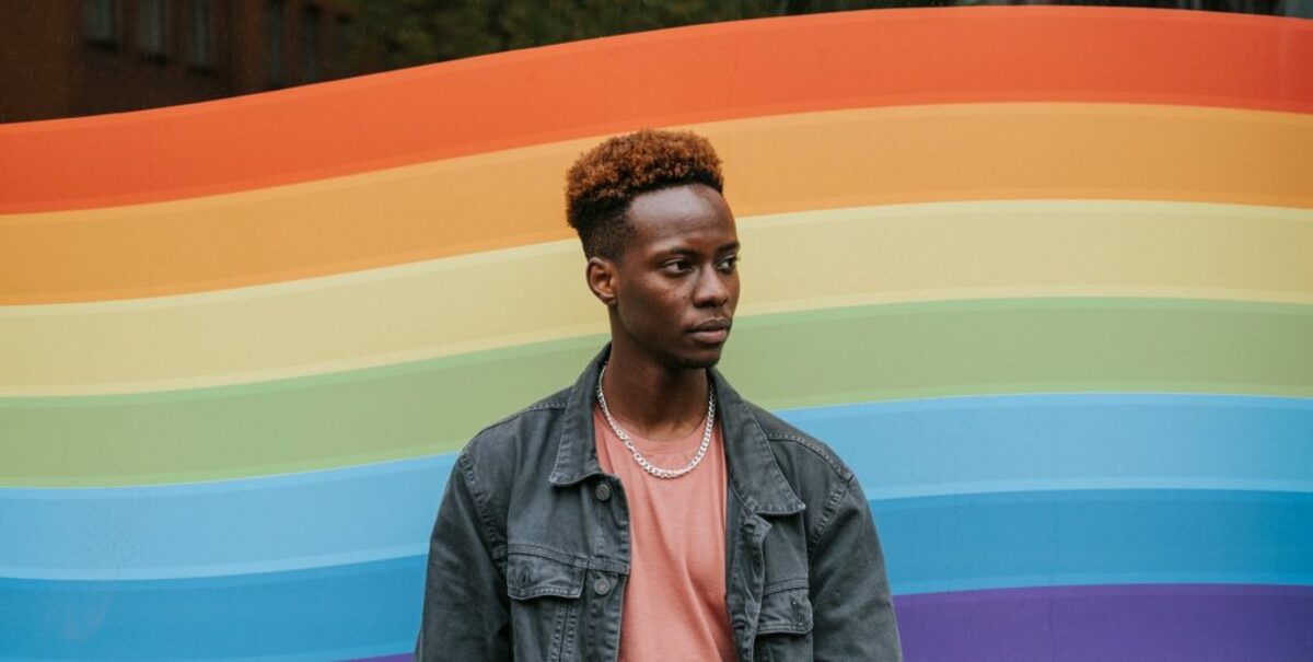 Contemplative black man standing against window painted in lgbt colors