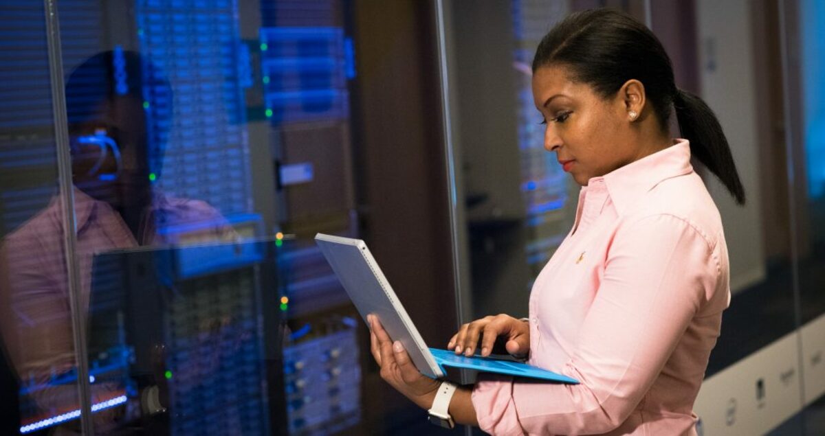 Photo of woman holding a gray laptop in front of systems