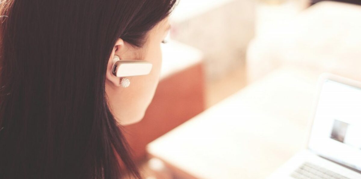 Woman wearing earpiece using white laptop computer