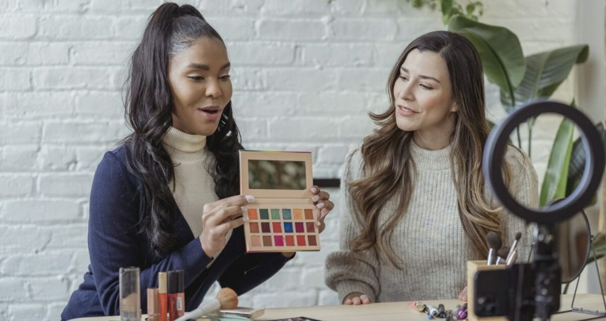 Young diverse ladies recording vlog about makeup products on smartphone