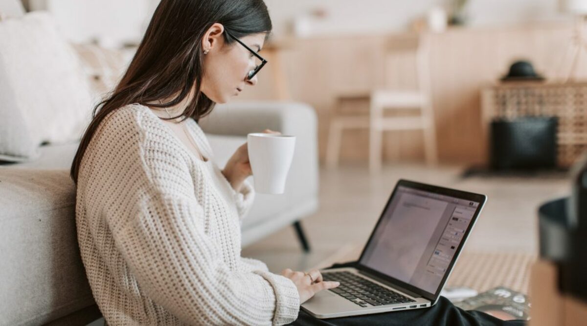 Content young businesswoman using laptop while taking tea cup at home