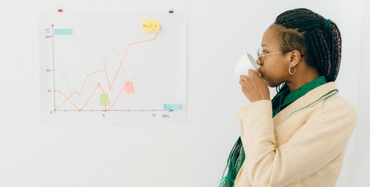 Woman in beige and white striped coat holding white ceramic mug while looking at the graph