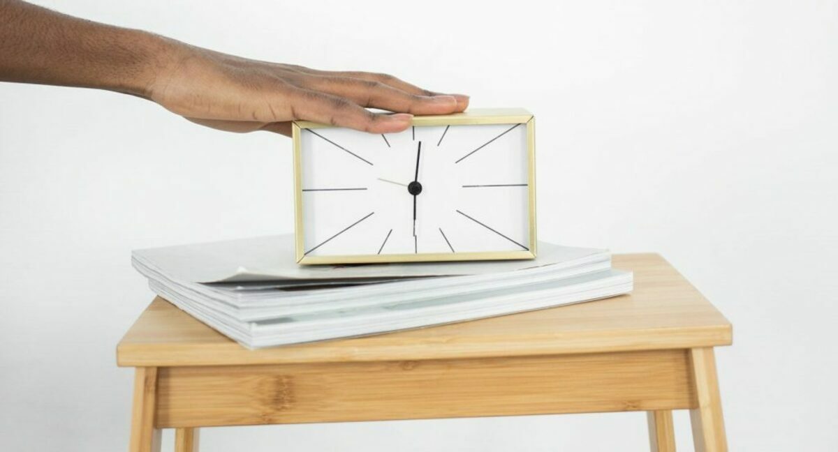 A person touching an analog clock on a wooden table