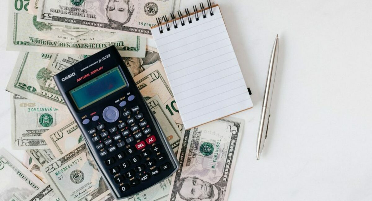 Calculator and notepad placed over stack of usa dollars