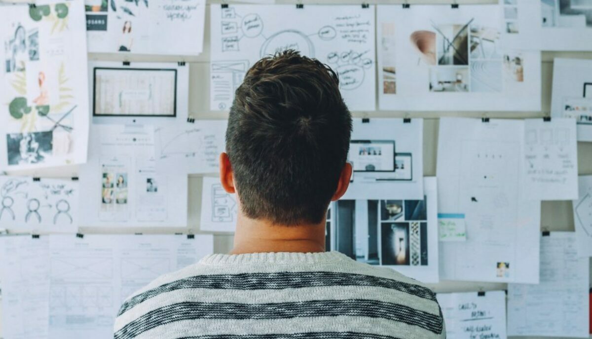 Man wearing black and white stripe shirt looking at white printer papers on the wall