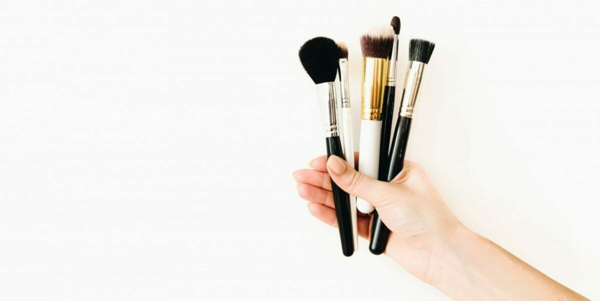 Various professional makeup brushes, held by a female caucasian MUA against white background