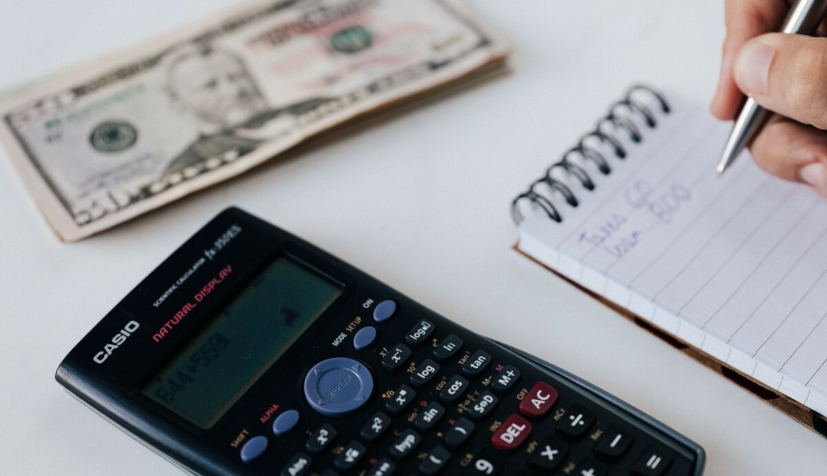 Crop unrecognizable accountant counting savings using notebook and calculator