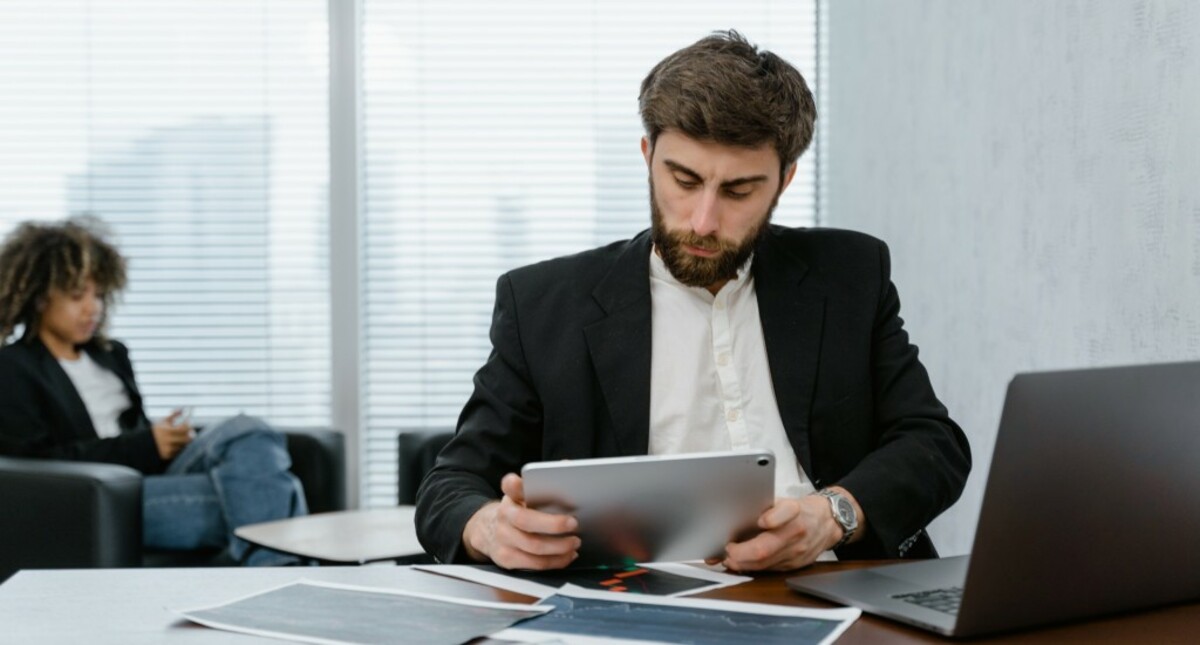 Man in black suit sitting while holding silver digital tablet