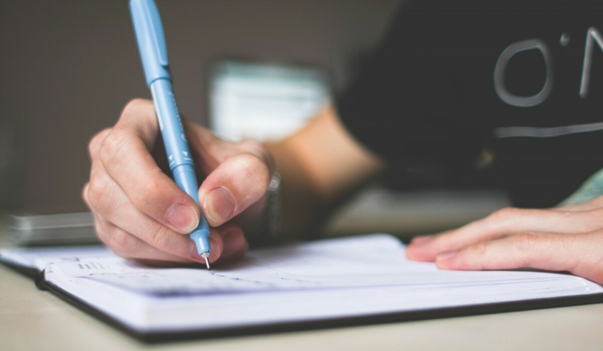 Person holding blue ballpoint pen writing in notebook