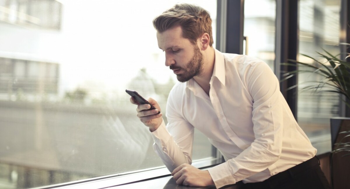 Photo of man in white dress shirt holding phone near window