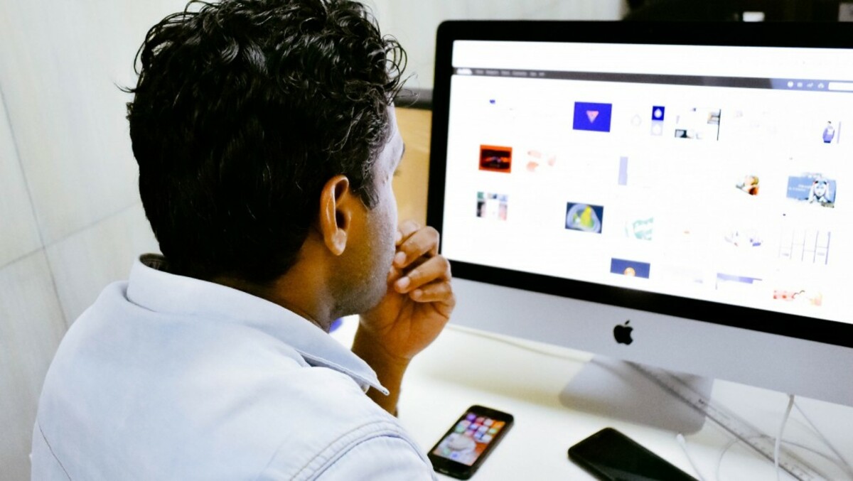 man sitting in front of silver Apple iMac on table