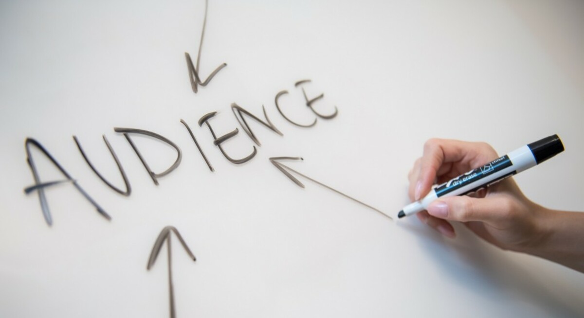 Woman's hand writing the word "audience" on a whiteboard, with arrows.