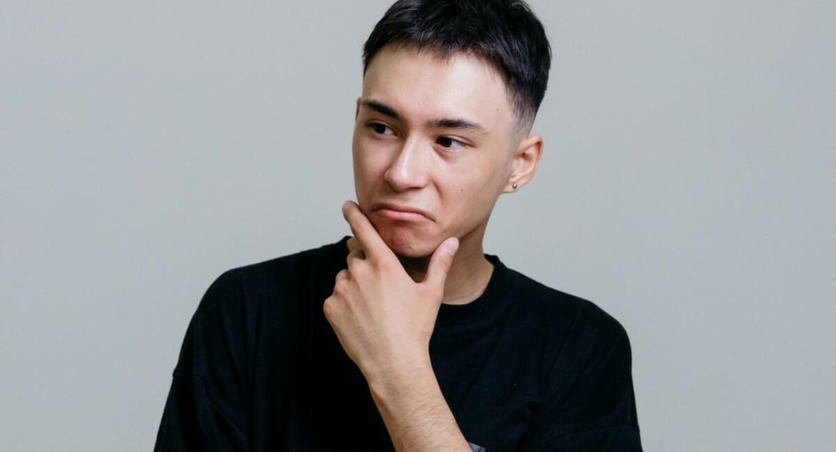 Man in black crew neck shirt thinking with his hand on his chin