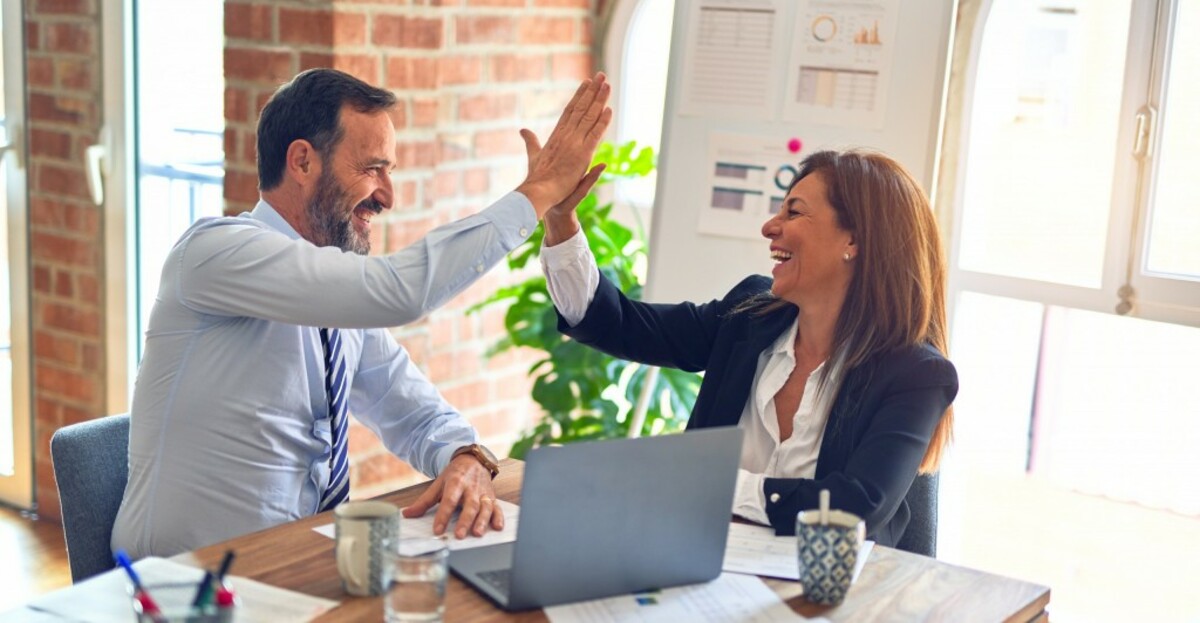 Two middle age business workers smiling happy and confident. Working together with smile on face hand giving high five at the office