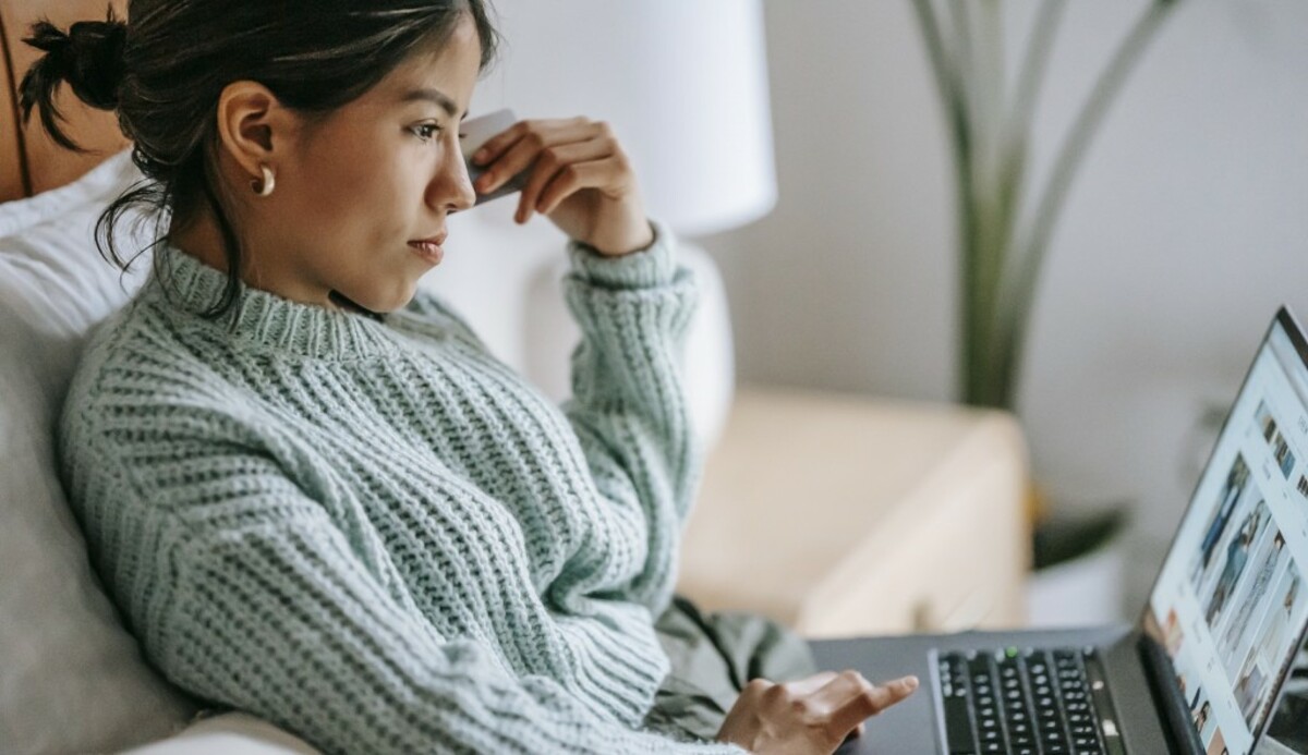 Focused young ethnic woman with credit card and laptop