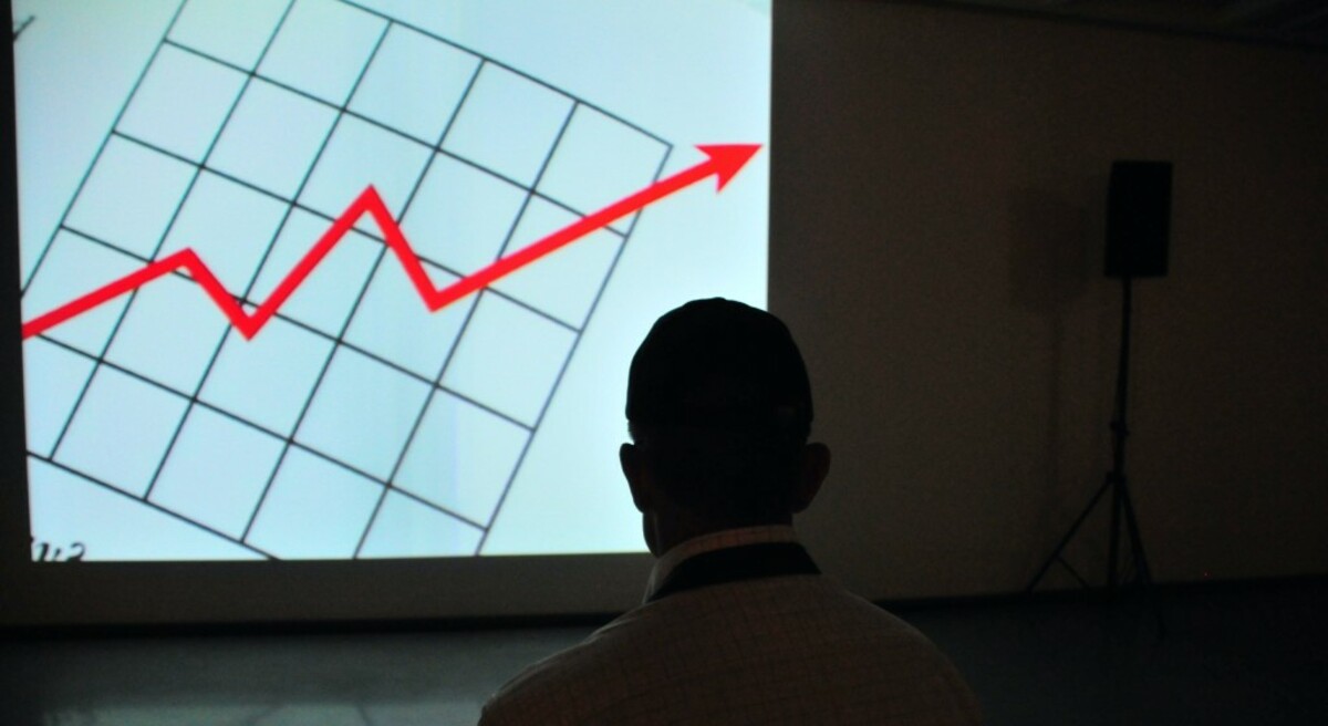 A man in front of a screen with a red arrow