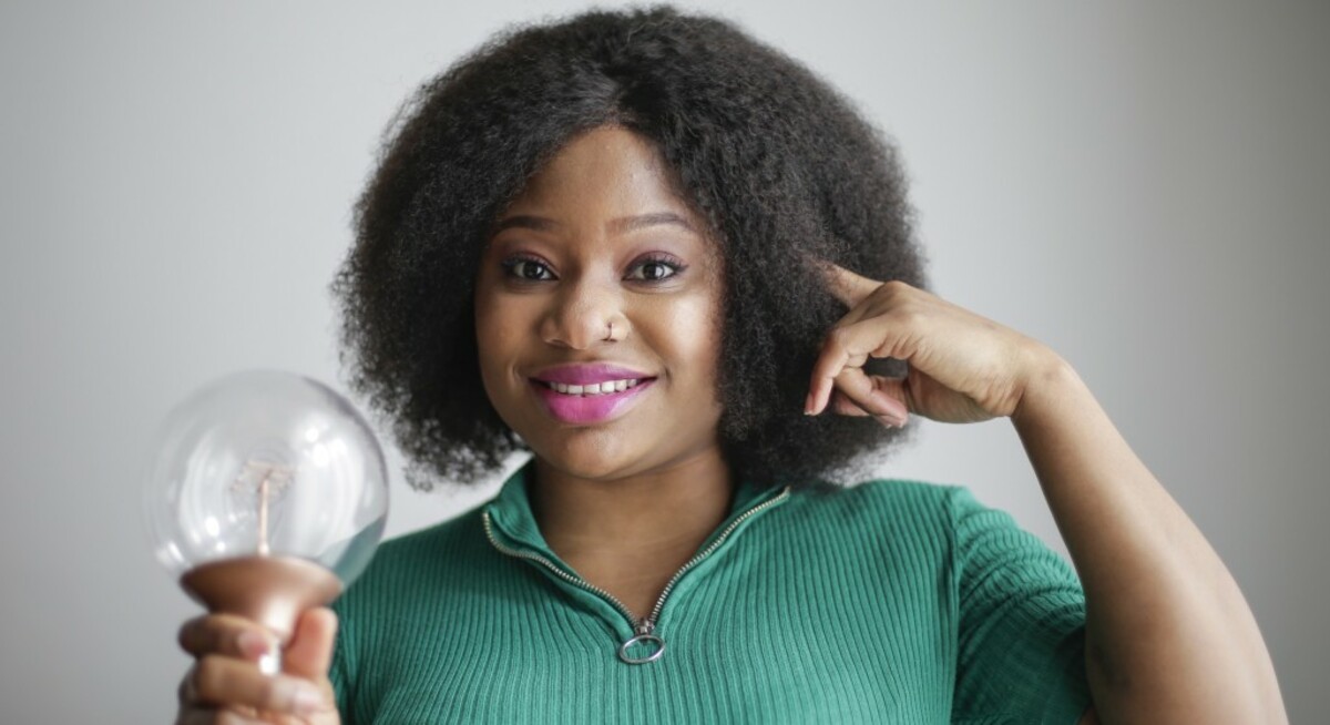 Positive young african american lady holding light bulb in hand on gray background