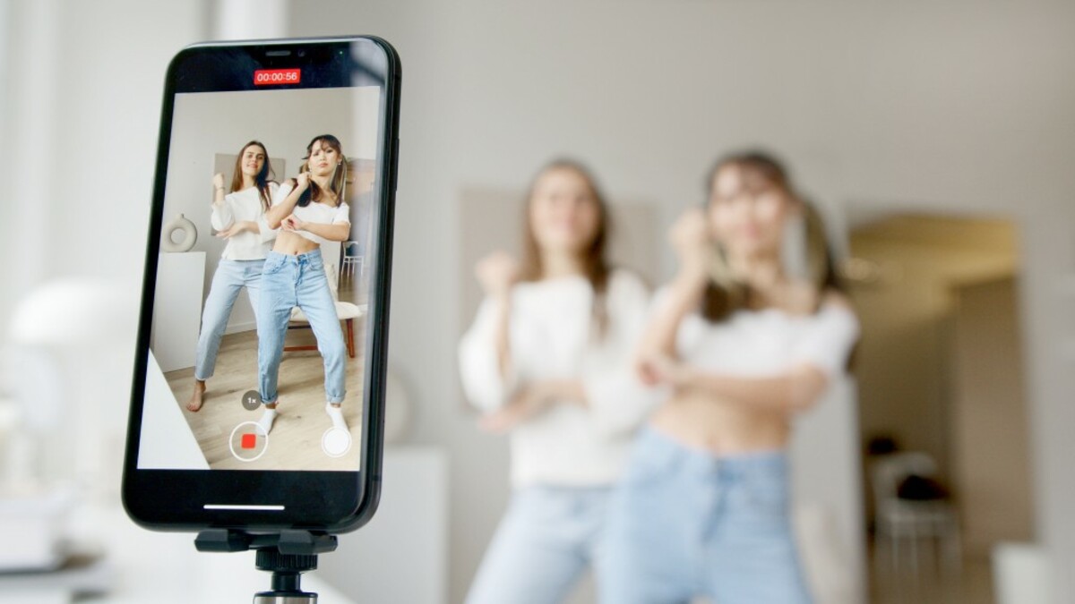 Woman in white sleeveless shirt and blue denim skirt holding black smartphone