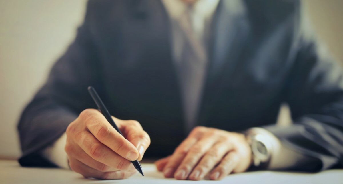 Crop businessman signing contract in office