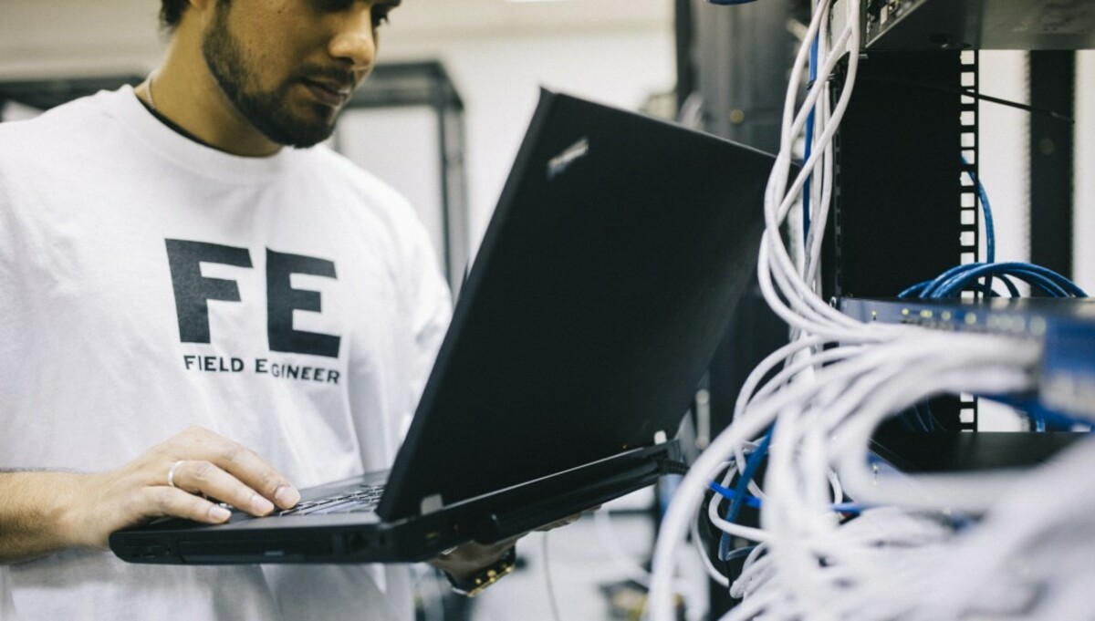 Serious ethnic field engineer examining hardware and working on laptop