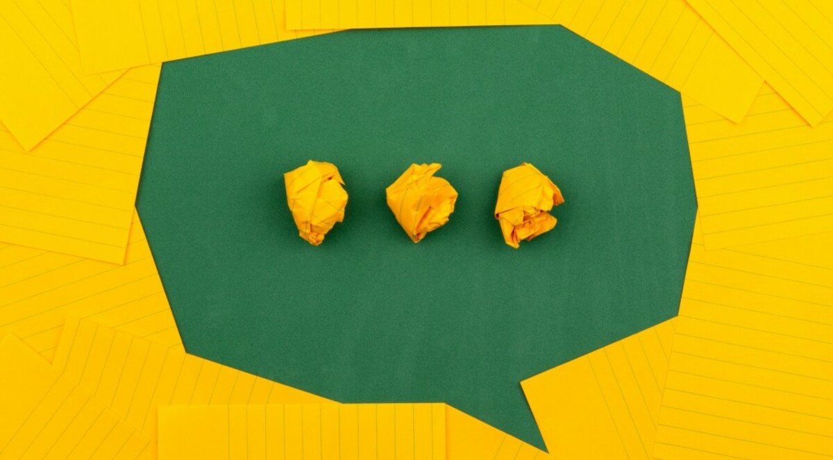 orange sheets of paper lie on a green school board and form a chat bubble with three crumpled papers.