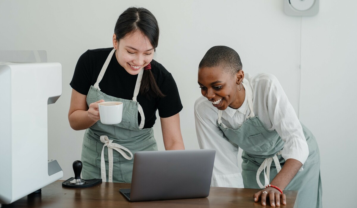 Young female baristas watching funny video on laptop during break